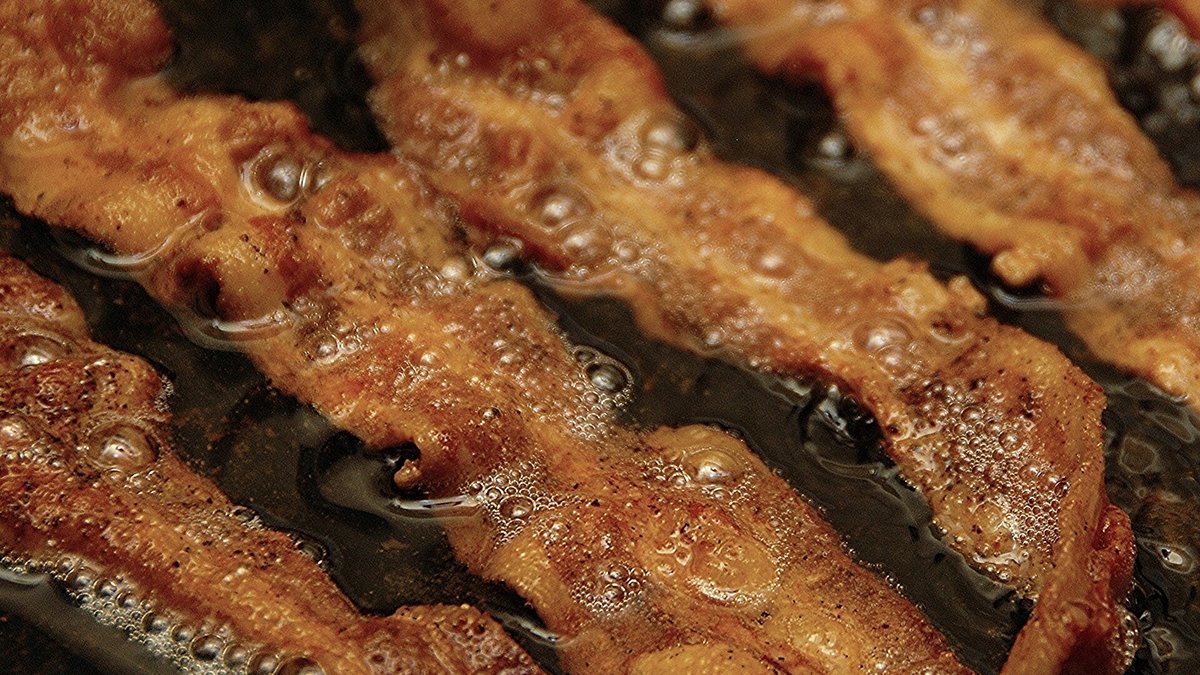 Close-up of strips of bacon frying in a pan of bubbling fat