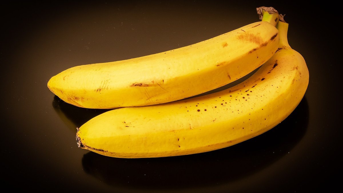 Two ripe yellow bananas on a dark background.