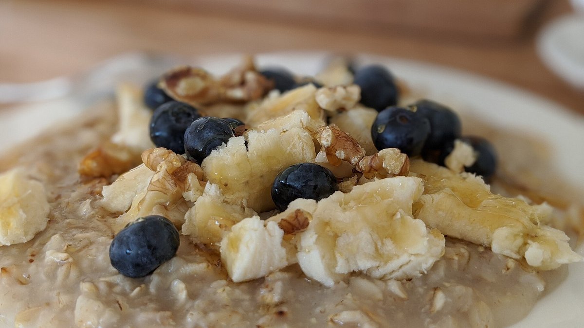 A bowl of oatmeal topped with sliced banana, blueberries and walnuts.